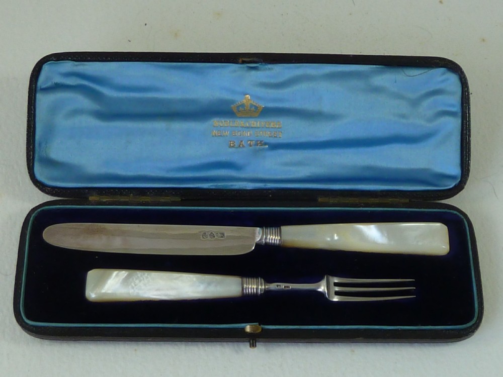 A boxed two-piece Georgian silver fruit knife and fork set with mother-of-pearl handles inside a blue velvet-lined case.