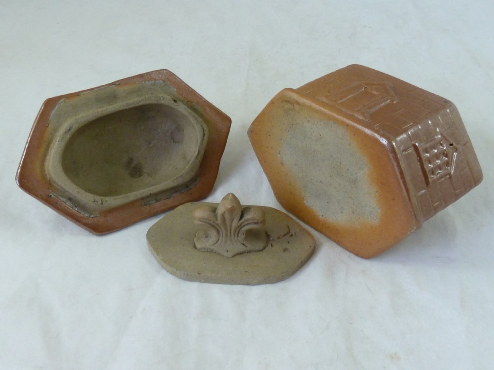 A warm brown salt-glazed stoneware tobacco jar shaped like a toll house cottage alongside its separate internal clay presser. View IV