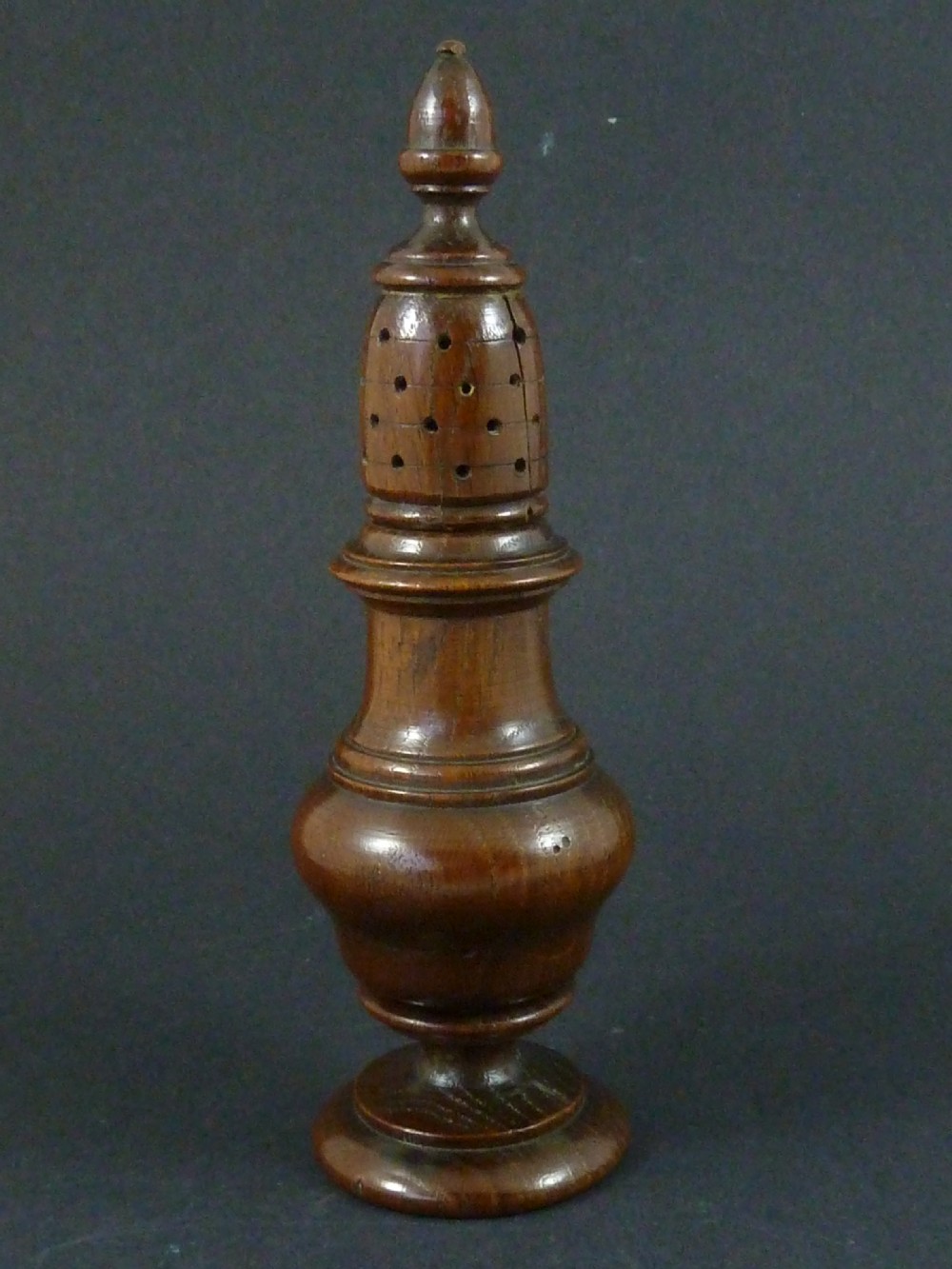 A turned dark wood sugar caster featuring a baluster form, pierced dome top with a finial, and a pedestal base. View II