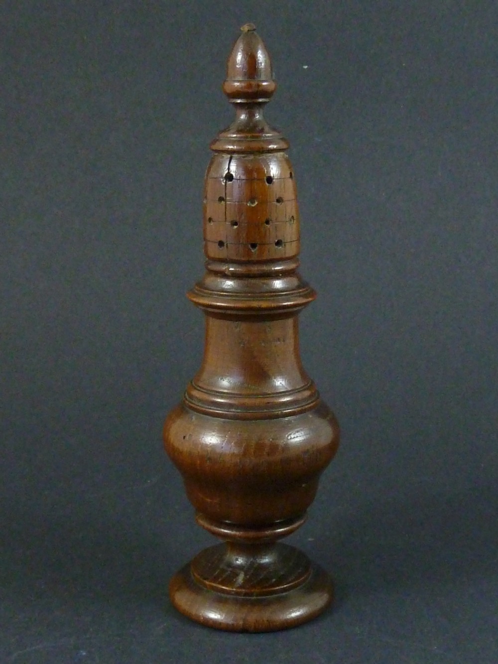 A turned dark wood sugar caster featuring a baluster form, pierced dome top with a finial, and a pedestal base. View III
