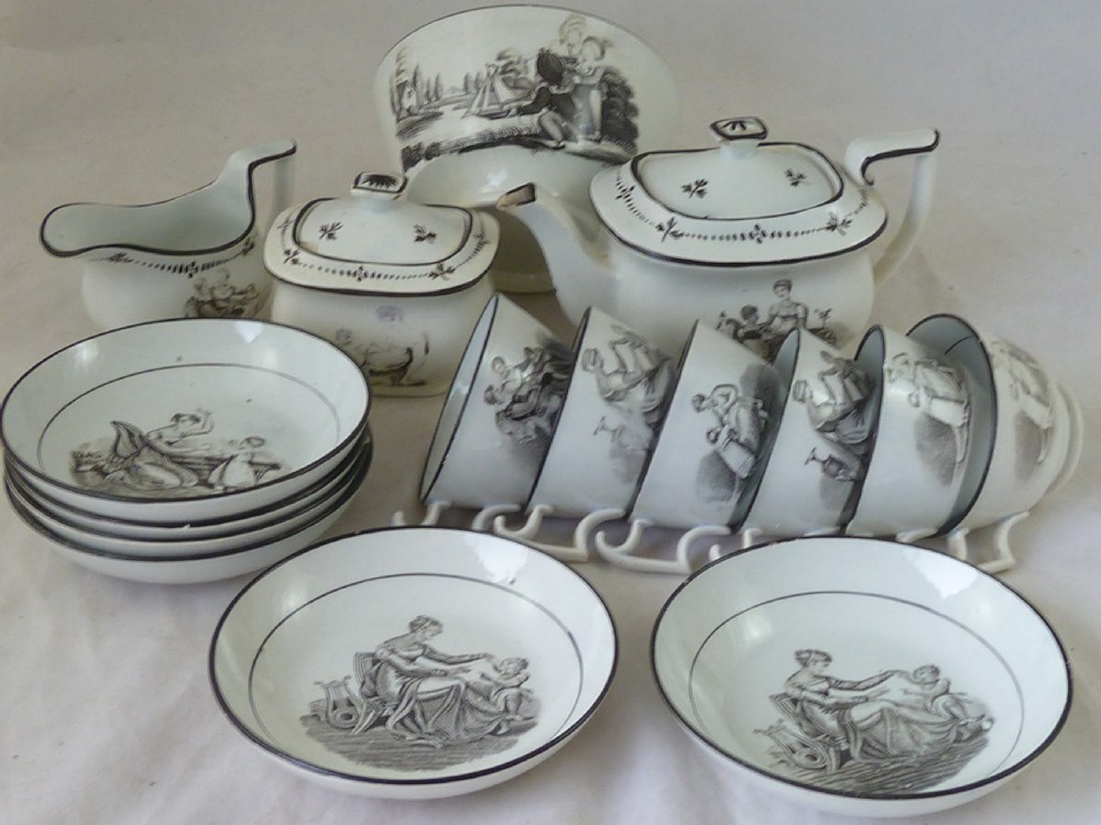 A Georgian era black transfer-printed miniature pearlware tea set featuring a teapot, sugar bowl, milk jug, bowls, cups, and saucers decorated with classical figural scenes.