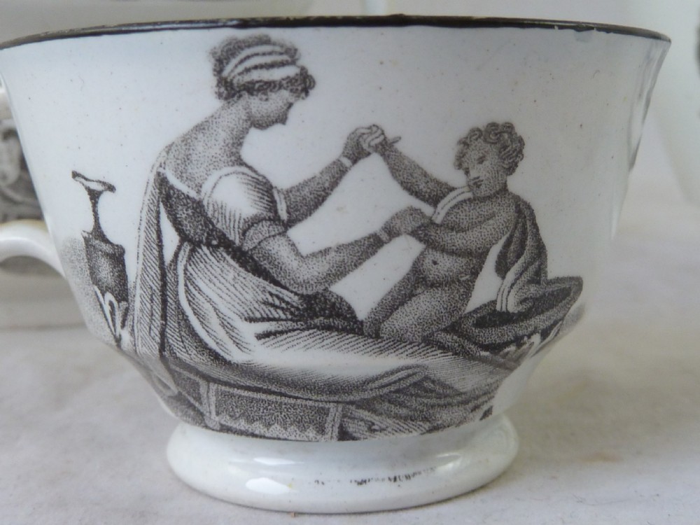 A Georgian era black transfer-printed miniature pearlware tea set featuring a teapot, sugar bowl, milk jug, bowls, cups, and saucers decorated with classical figural scenes. View VIII