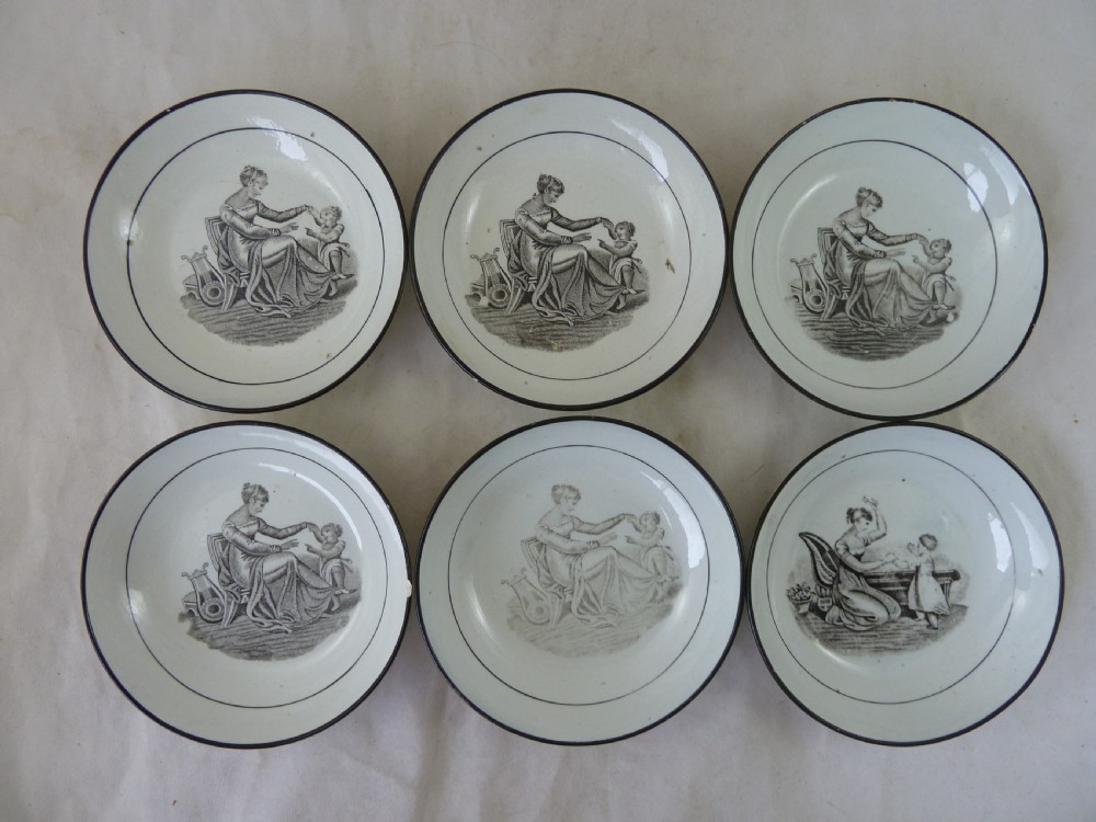 A Georgian era black transfer-printed miniature pearlware tea set featuring a teapot, sugar bowl, milk jug, bowls, cups, and saucers decorated with classical figural scenes. View XXI