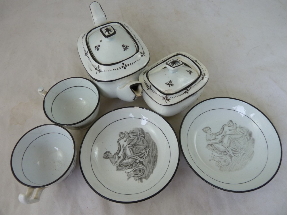 A Georgian era black transfer-printed miniature pearlware tea set featuring a teapot, sugar bowl, milk jug, bowls, cups, and saucers decorated with classical figural scenes. View XXV