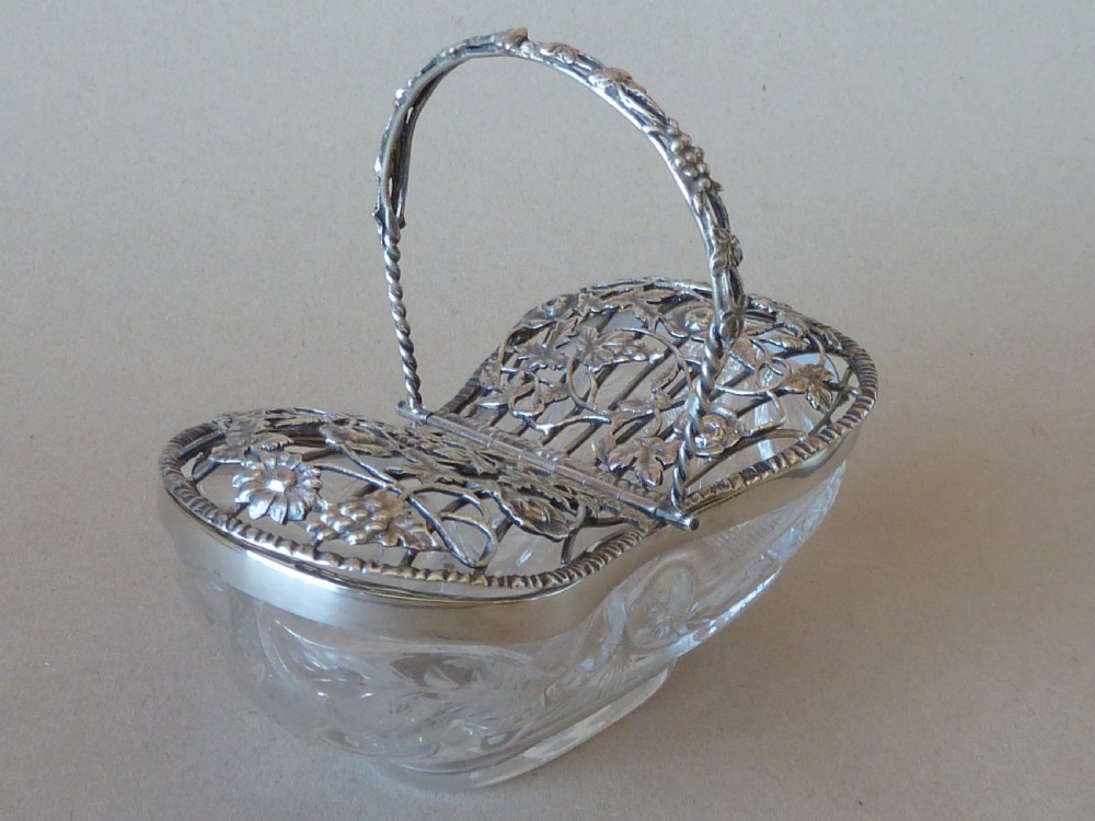 An oval clear cut glass bowl with a pierced silver floral lid and an overhead swing handle. View III