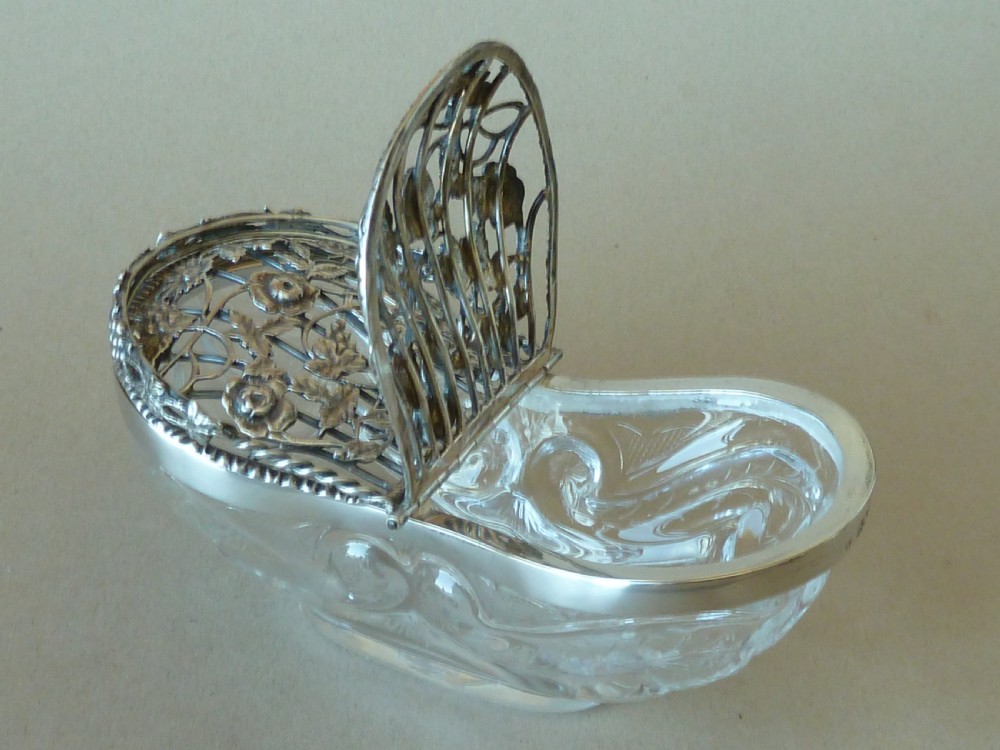 An oval clear cut glass bowl with a pierced silver floral lid and an overhead swing handle. View IV