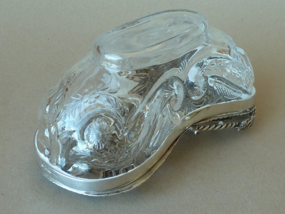 An oval clear cut glass bowl with a pierced silver floral lid and an overhead swing handle. View VII