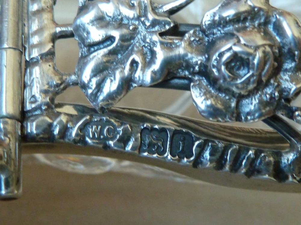 An oval clear cut glass bowl with a pierced silver floral lid and an overhead swing handle. View IX