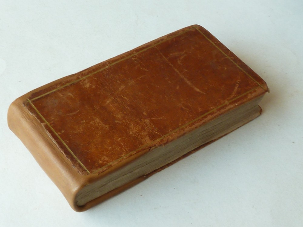 A small antique leatherbound book with a brown calfskin cover featuring gilt border tooling and aged paper edges.