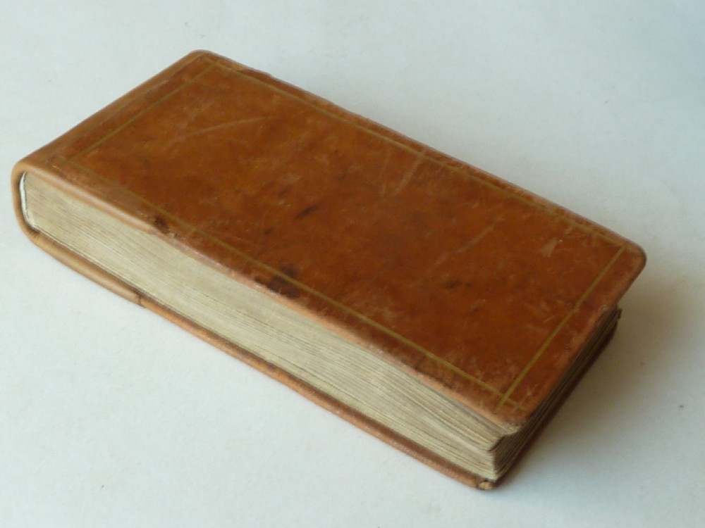 A small antique leatherbound book with a brown calfskin cover featuring gilt border tooling and aged paper edges. View III