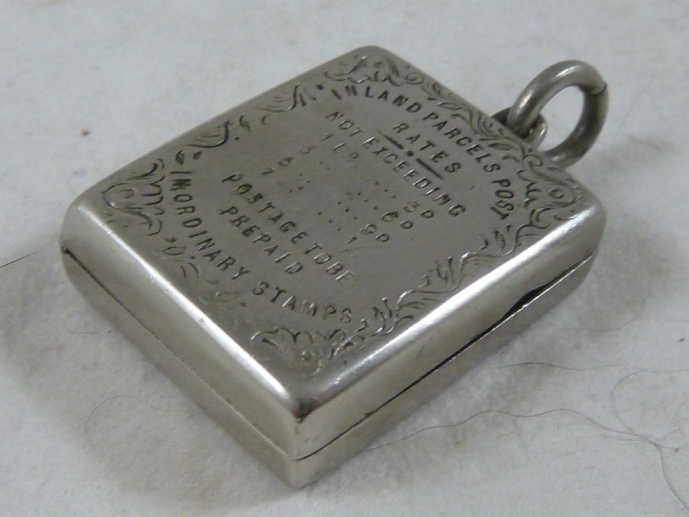 A rectangular Victorian silver-coloured metal stamp case fob featuring engraved scrollwork borders and etched text displaying inland parcel post rates. View III
