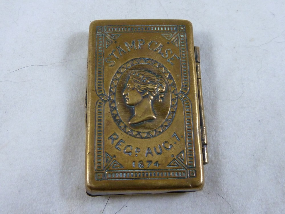 A small rectangular Victorian brass pocket stamp case embossed with a portrait of Queen Victoria and registration text dated 1874.