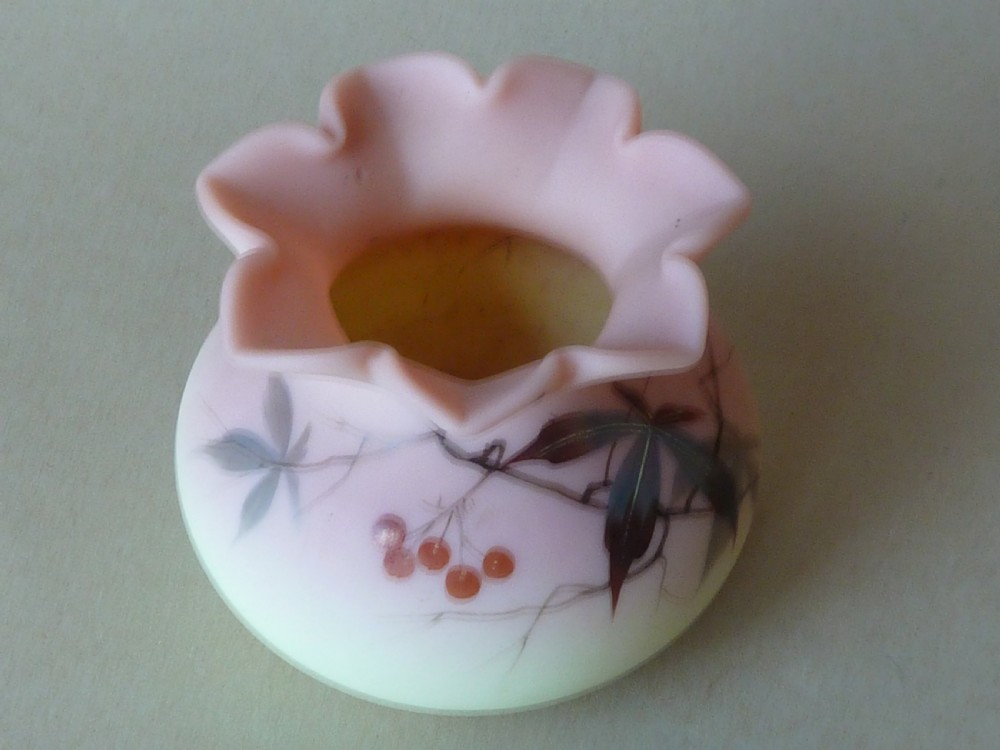 A small Victorian Burmese satin glass vase with a crimped rim, shading from yellow at the base to pink at the top, decorated with hand-painted leaves and berries. View V