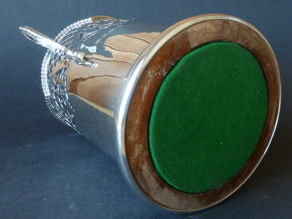 A solid silver magnum wine bottle holder featuring pierced fretwork detail, two beaded scroll handles, and British hallmarks on the side. View IV