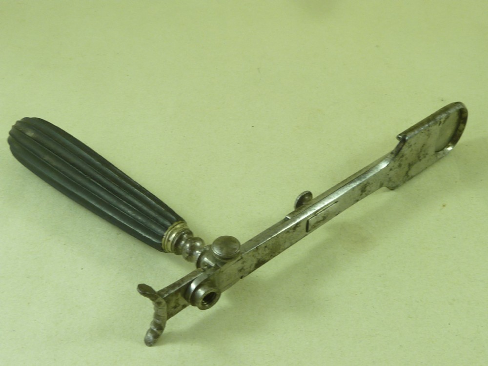 An antique metal tonsil guillotine featuring a long steel shaft with a sliding blade mechanism and a fluted black ebony handle. View II
