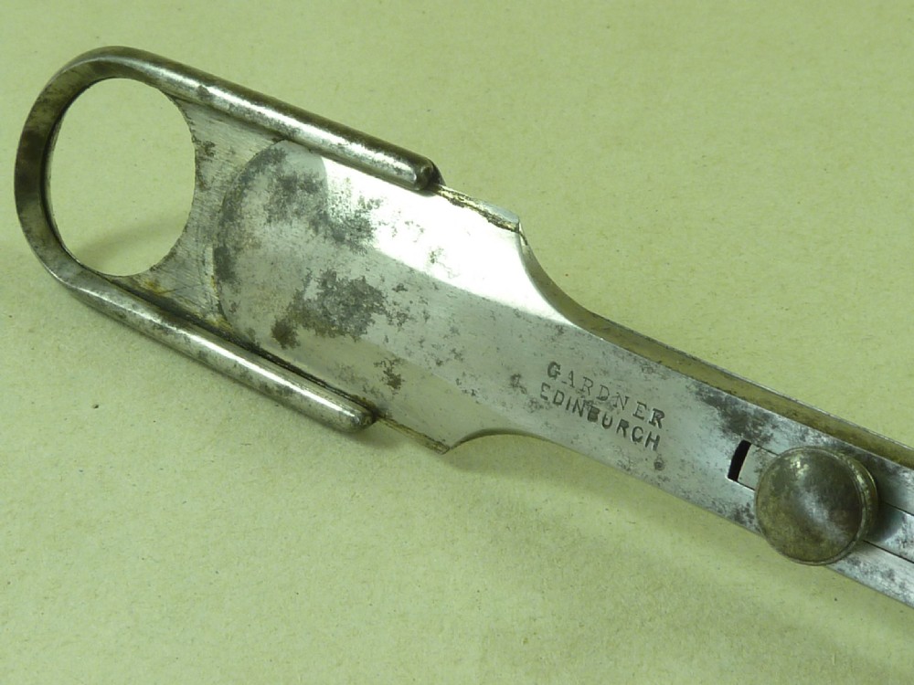 An antique metal tonsil guillotine featuring a long steel shaft with a sliding blade mechanism and a fluted black ebony handle. View III