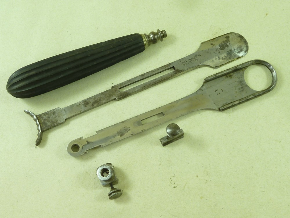 An antique metal tonsil guillotine featuring a long steel shaft with a sliding blade mechanism and a fluted black ebony handle. View V