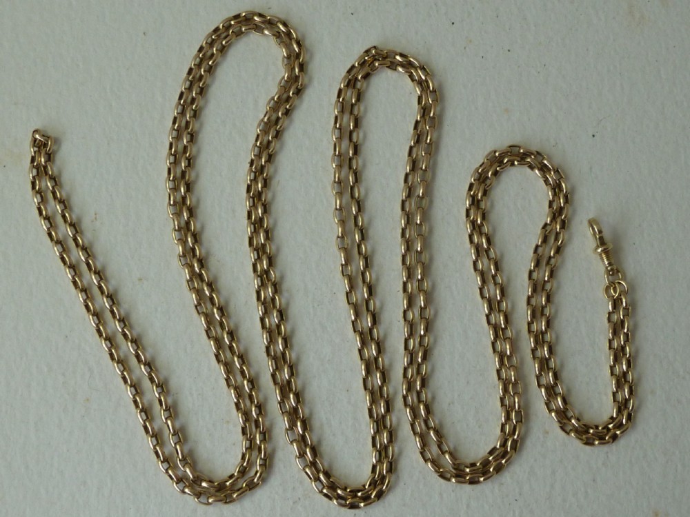 A long 14ct yellow gold Victorian guard chain featuring interlocking oval links and a dog clip clasp, laid flat against a neutral surface.