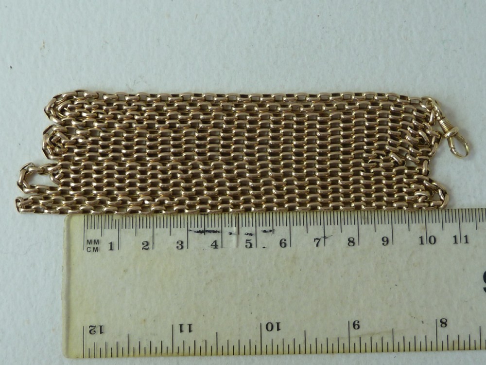 A long 14ct yellow gold Victorian guard chain featuring interlocking oval links and a dog clip clasp, laid flat against a neutral surface. View IV