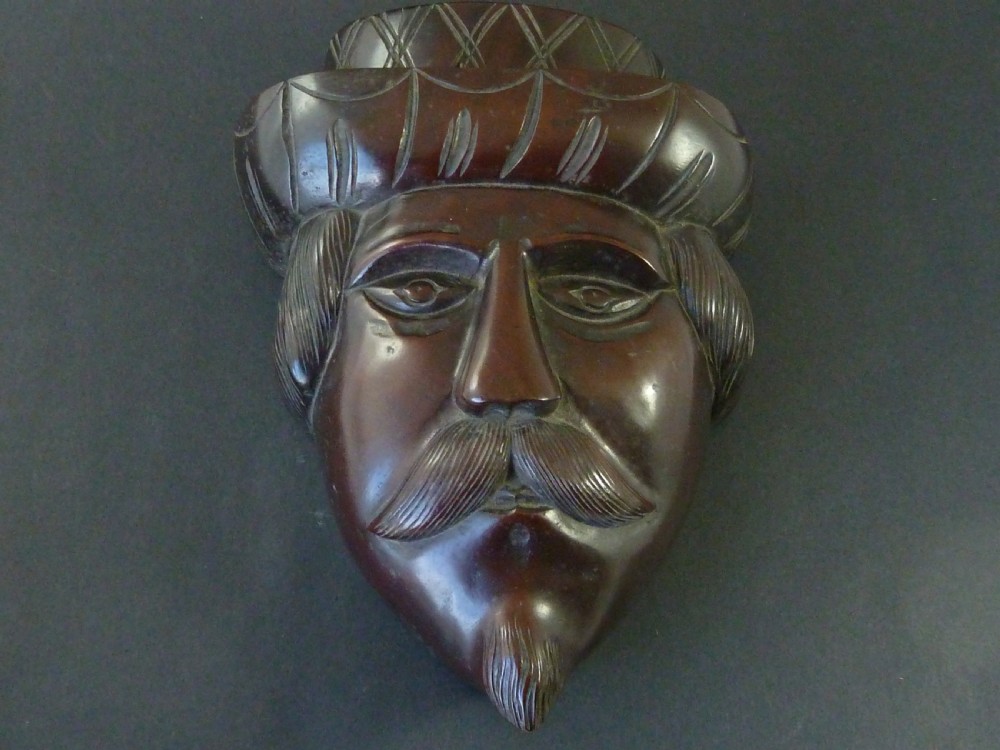 A polished dark hardwood wall mask depicting a turbaned man with a detailed moustache and beard.