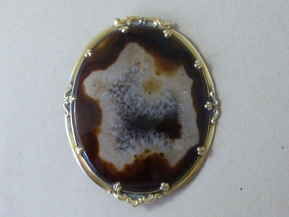An oval Victorian brooch featuring a translucent brown and white patterned agate stone set within a gold-toned metal frame with decorative prongs.