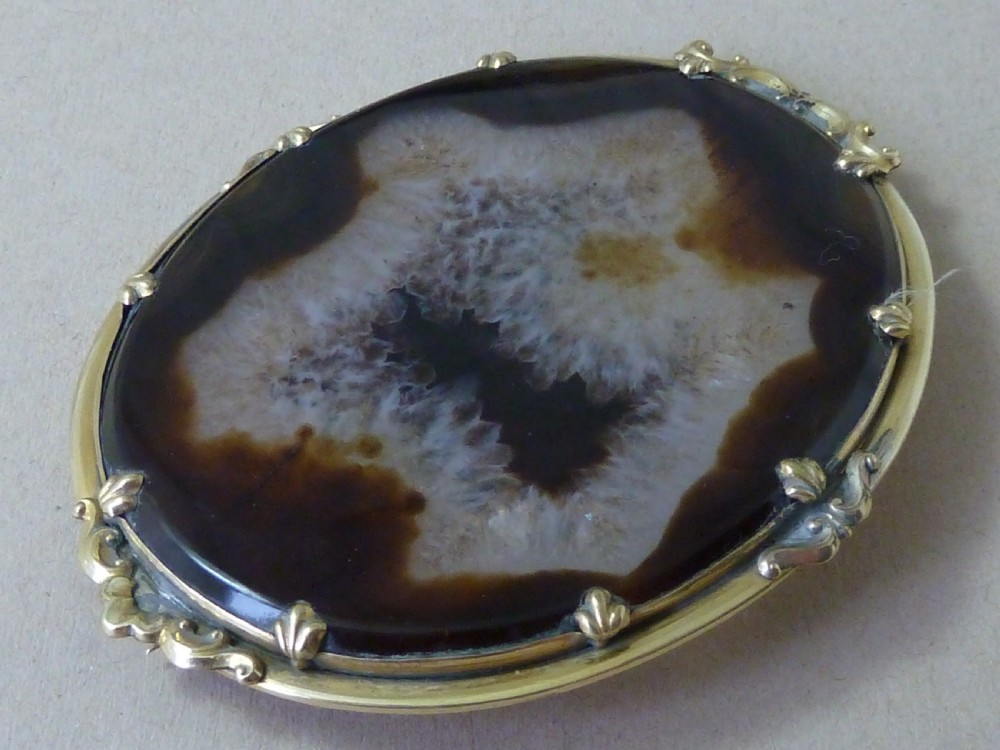 An oval Victorian brooch featuring a translucent brown and white patterned agate stone set within a gold-toned metal frame with decorative prongs. View II