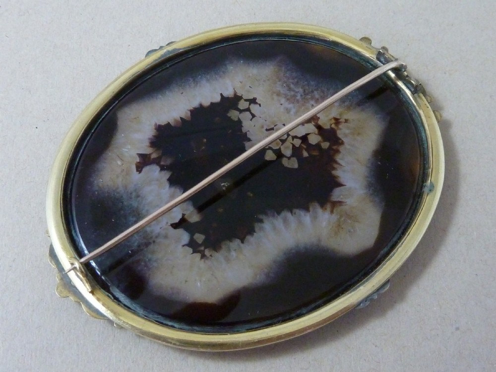 An oval Victorian brooch featuring a translucent brown and white patterned agate stone set within a gold-toned metal frame with decorative prongs. View III