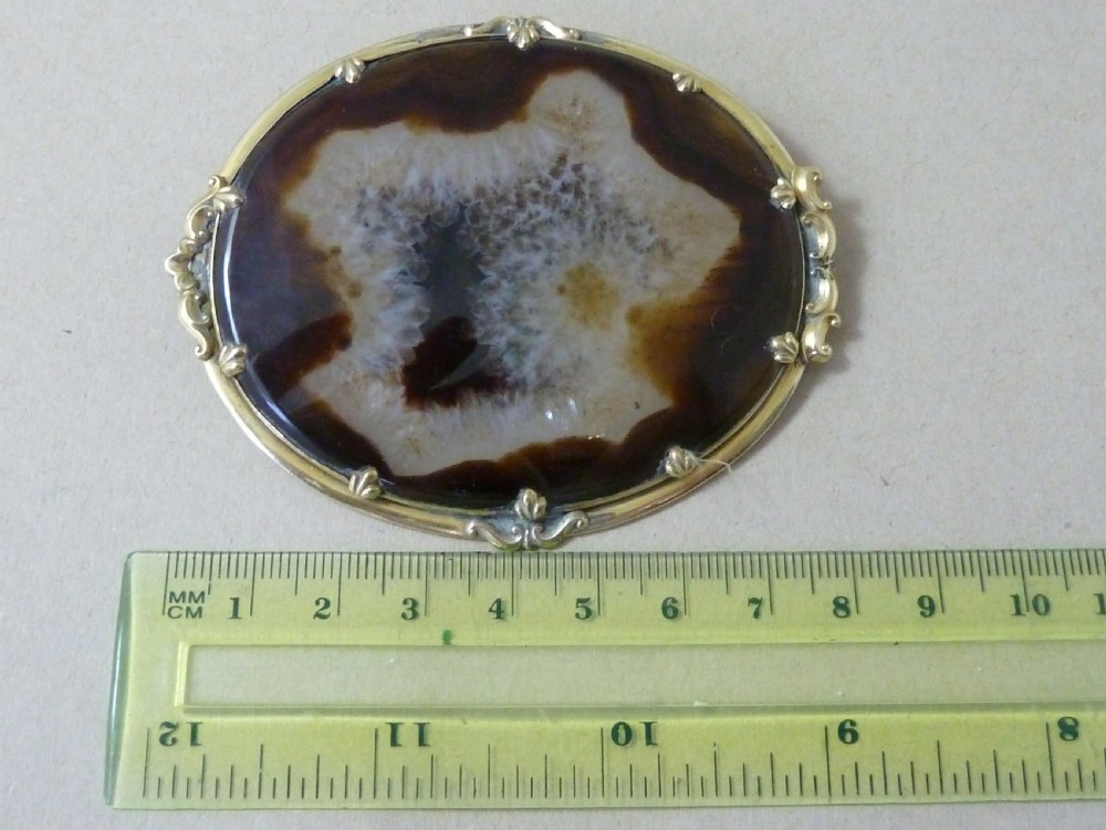 An oval Victorian brooch featuring a translucent brown and white patterned agate stone set within a gold-toned metal frame with decorative prongs. View IV