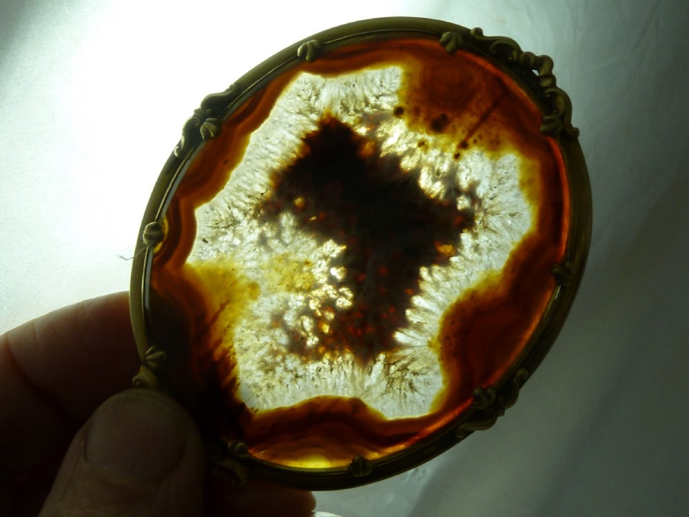 An oval Victorian brooch featuring a translucent brown and white patterned agate stone set within a gold-toned metal frame with decorative prongs. View V