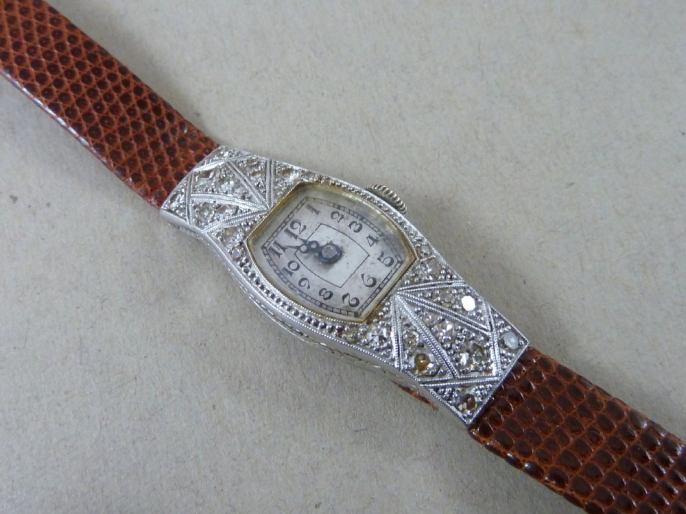 An Art Deco ladies cocktail watch with a white gold diamond-set geometric case, a cream dial, and a brown textured leather strap.