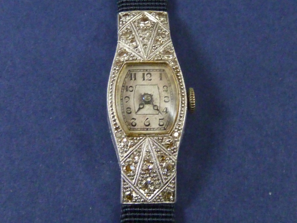 An Art Deco ladies cocktail watch with a white gold diamond-set geometric case, a cream dial, and a brown textured leather strap. View V