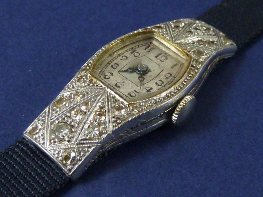 An Art Deco ladies cocktail watch with a white gold diamond-set geometric case, a cream dial, and a brown textured leather strap. View VII