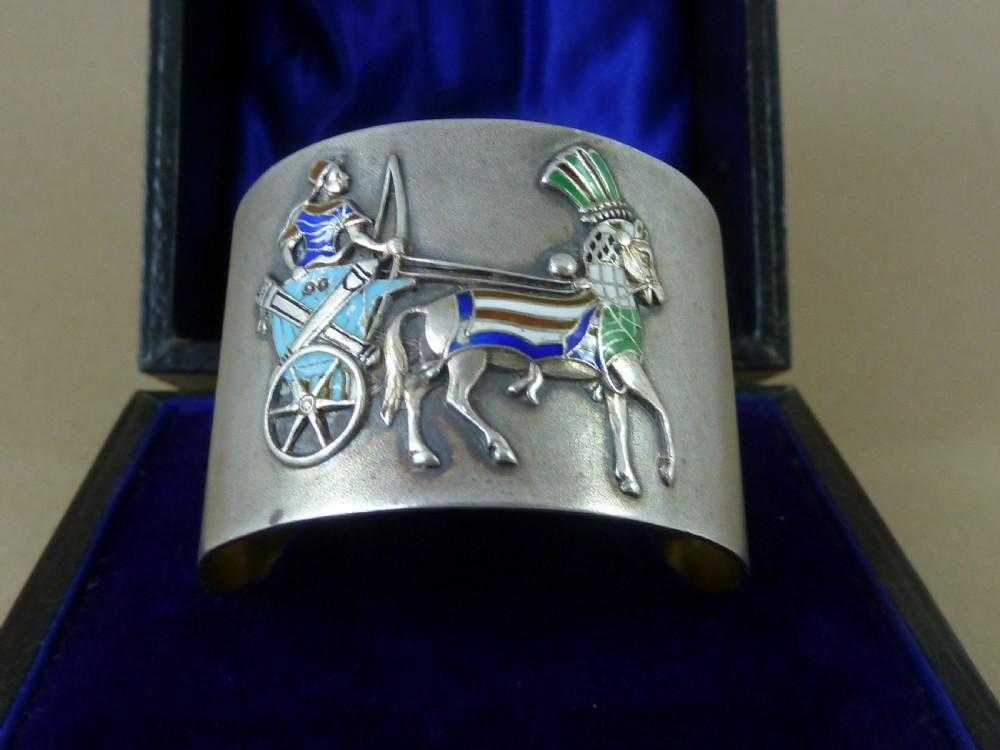 A curved 800 silver napkin ring featuring a detailed enamel relief depiction of a charioteer driving a horse in blue and green tones.