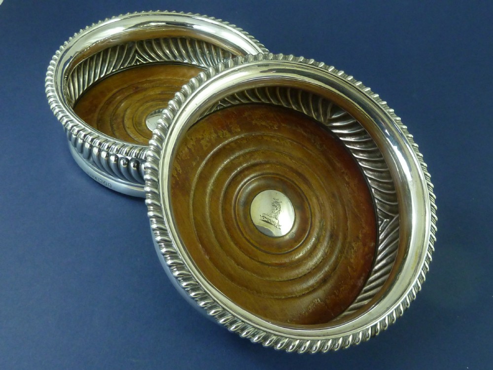 A pair of round Georgian sterling silver wine coasters with gadrooned rims, turned wooden bases, and central engraved silver bosses.