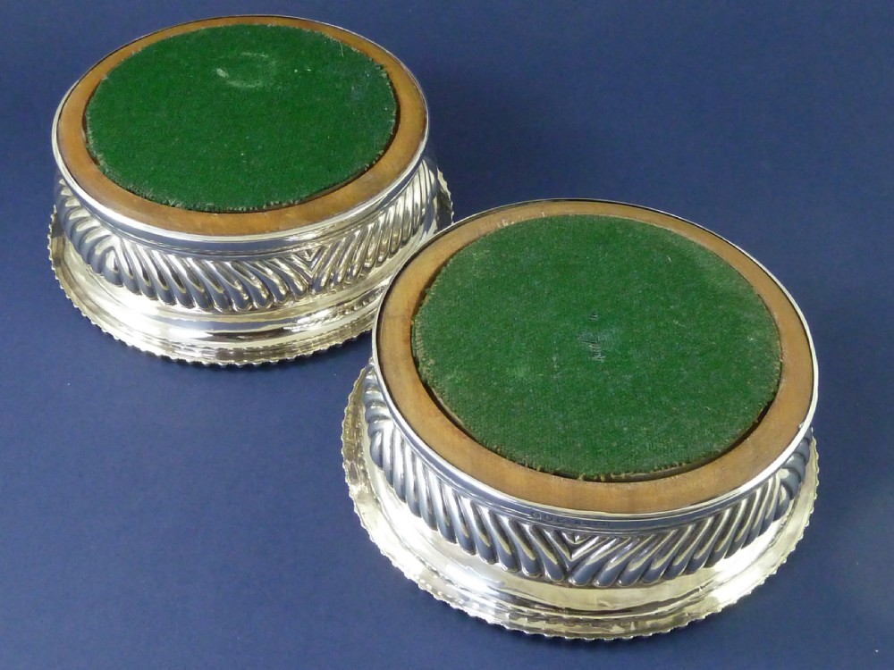 A pair of round Georgian sterling silver wine coasters with gadrooned rims, turned wooden bases, and central engraved silver bosses. View V