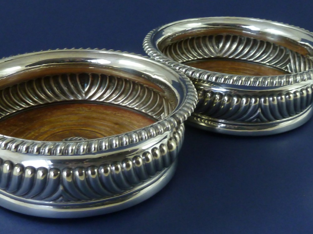 A pair of round Georgian sterling silver wine coasters with gadrooned rims, turned wooden bases, and central engraved silver bosses. View VI
