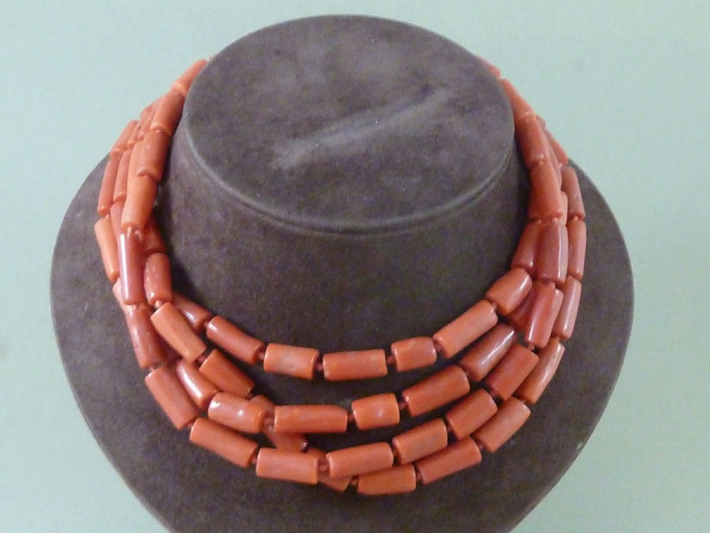 A long strand of cylindrical red coral beads wrapped multiple times around a display stand.
