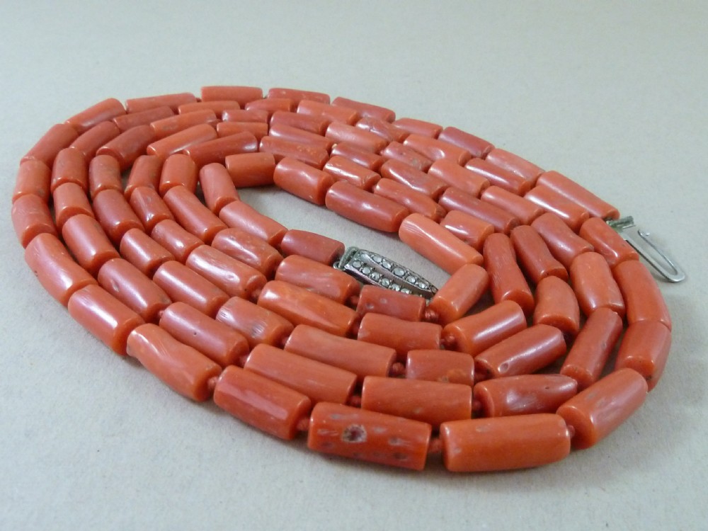 A long strand of cylindrical red coral beads wrapped multiple times around a display stand. View II