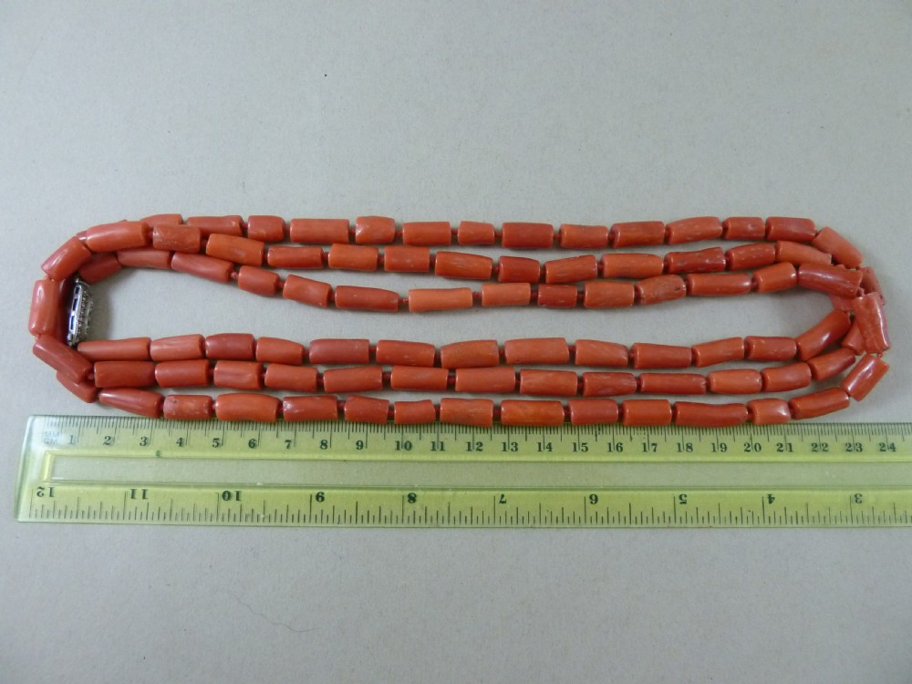 A long strand of cylindrical red coral beads wrapped multiple times around a display stand. View III