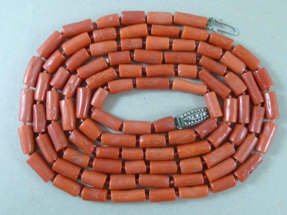A long strand of cylindrical red coral beads wrapped multiple times around a display stand. View IV