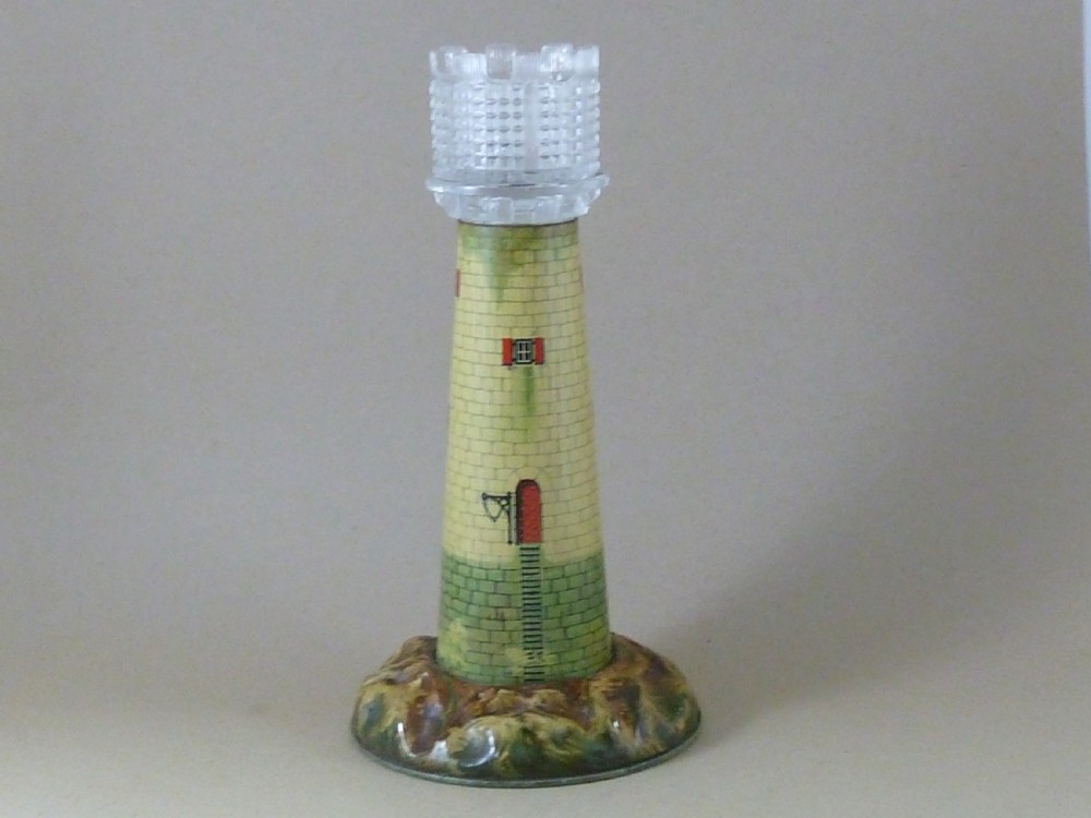 A Victorian lithographed tin candle holder shaped like a lighthouse with a clear pressed glass lantern shade.