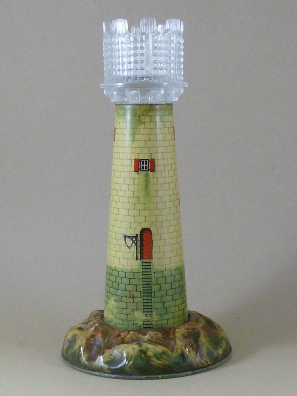 A Victorian lithographed tin candle holder shaped like a lighthouse with a clear pressed glass lantern shade. View II