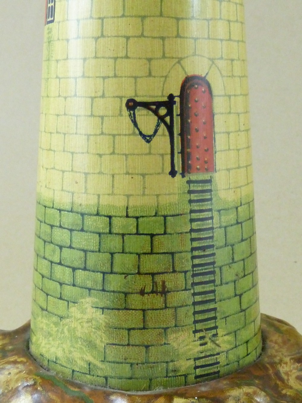 A Victorian lithographed tin candle holder shaped like a lighthouse with a clear pressed glass lantern shade. View III