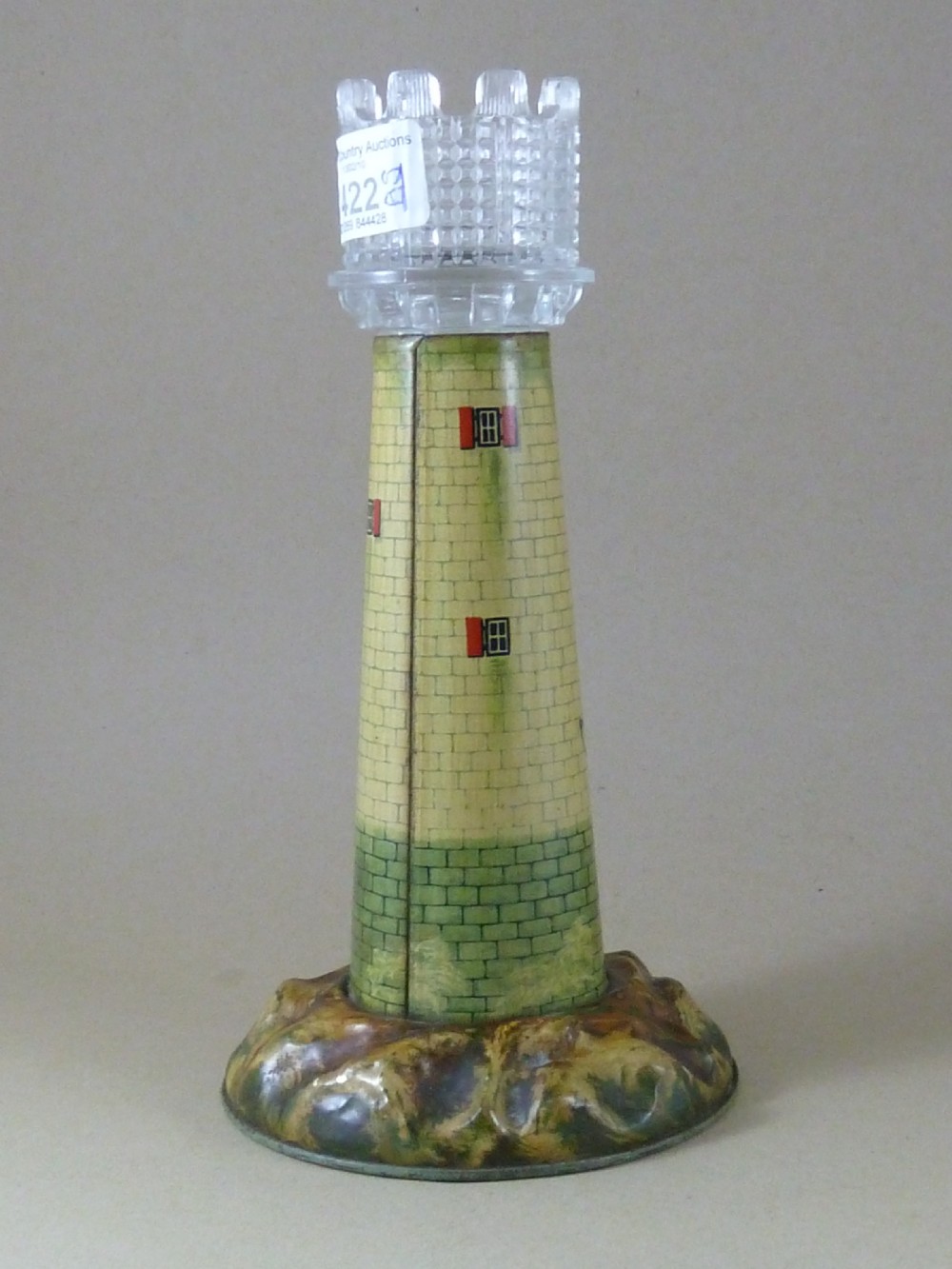 A Victorian lithographed tin candle holder shaped like a lighthouse with a clear pressed glass lantern shade. View IV