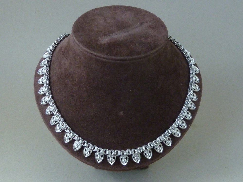 An Edwardian sterling silver collar necklace featuring a round link chain suspended with pierced heart-shaped fringe pendants.