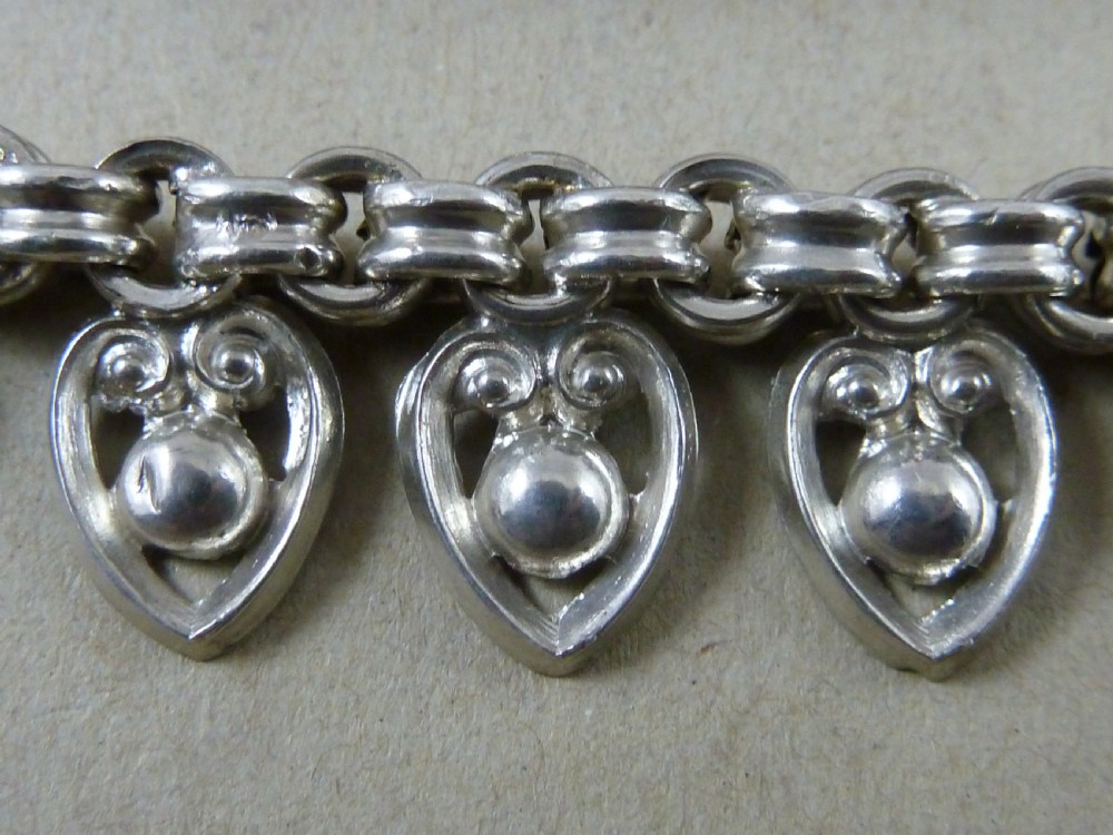 An Edwardian sterling silver collar necklace featuring a round link chain suspended with pierced heart-shaped fringe pendants. View V