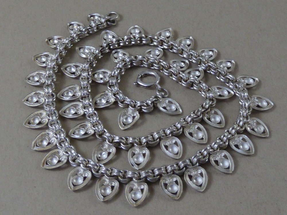 An Edwardian sterling silver collar necklace featuring a round link chain suspended with pierced heart-shaped fringe pendants. View VII