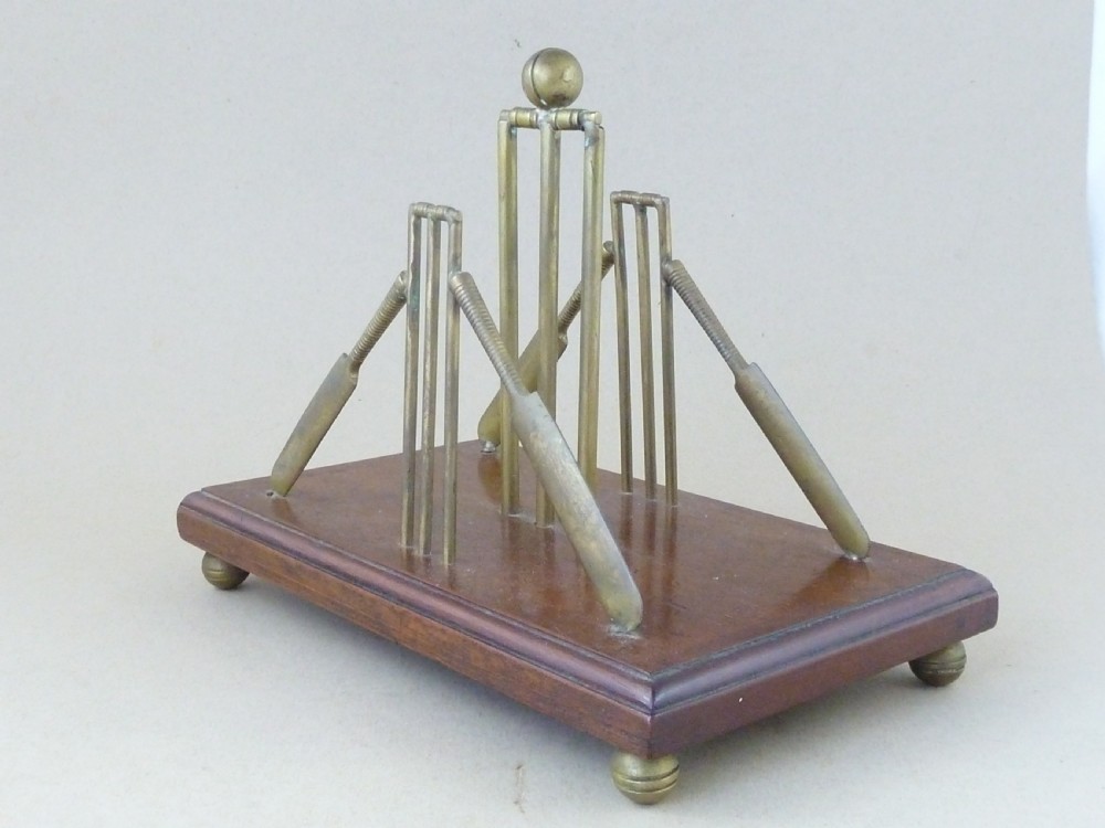 An antique brass letter rack shaped as miniature cricket bats, wickets, and a ball mounted on a rectangular mahogany wooden base with small bun feet. View III