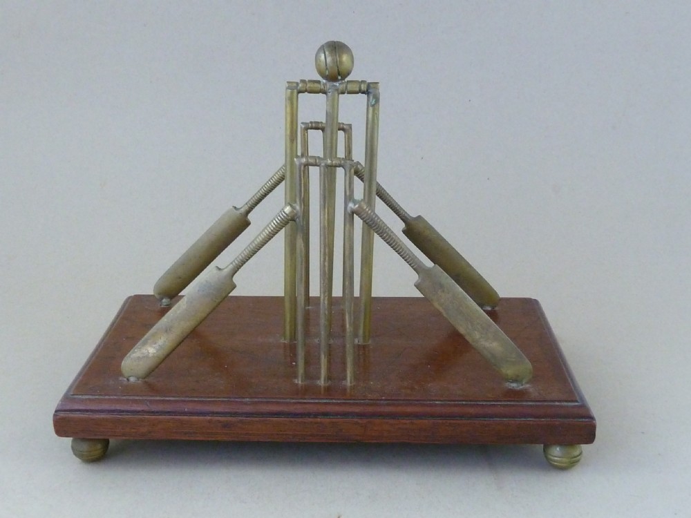 An antique brass letter rack shaped as miniature cricket bats, wickets, and a ball mounted on a rectangular mahogany wooden base with small bun feet. View IV