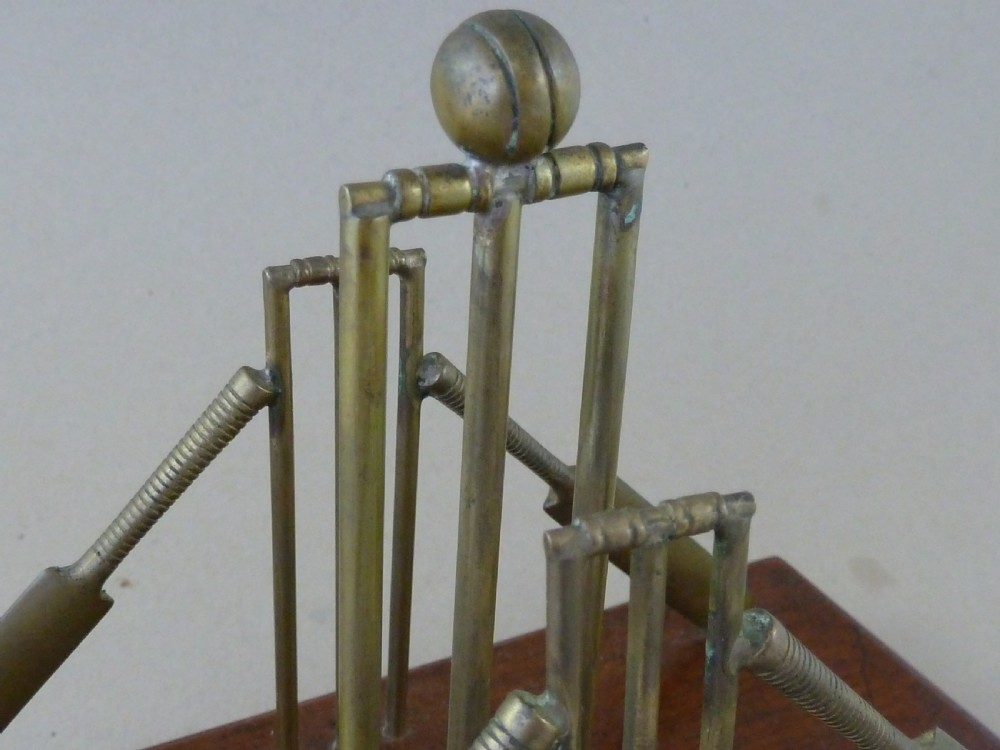 An antique brass letter rack shaped as miniature cricket bats, wickets, and a ball mounted on a rectangular mahogany wooden base with small bun feet. View V